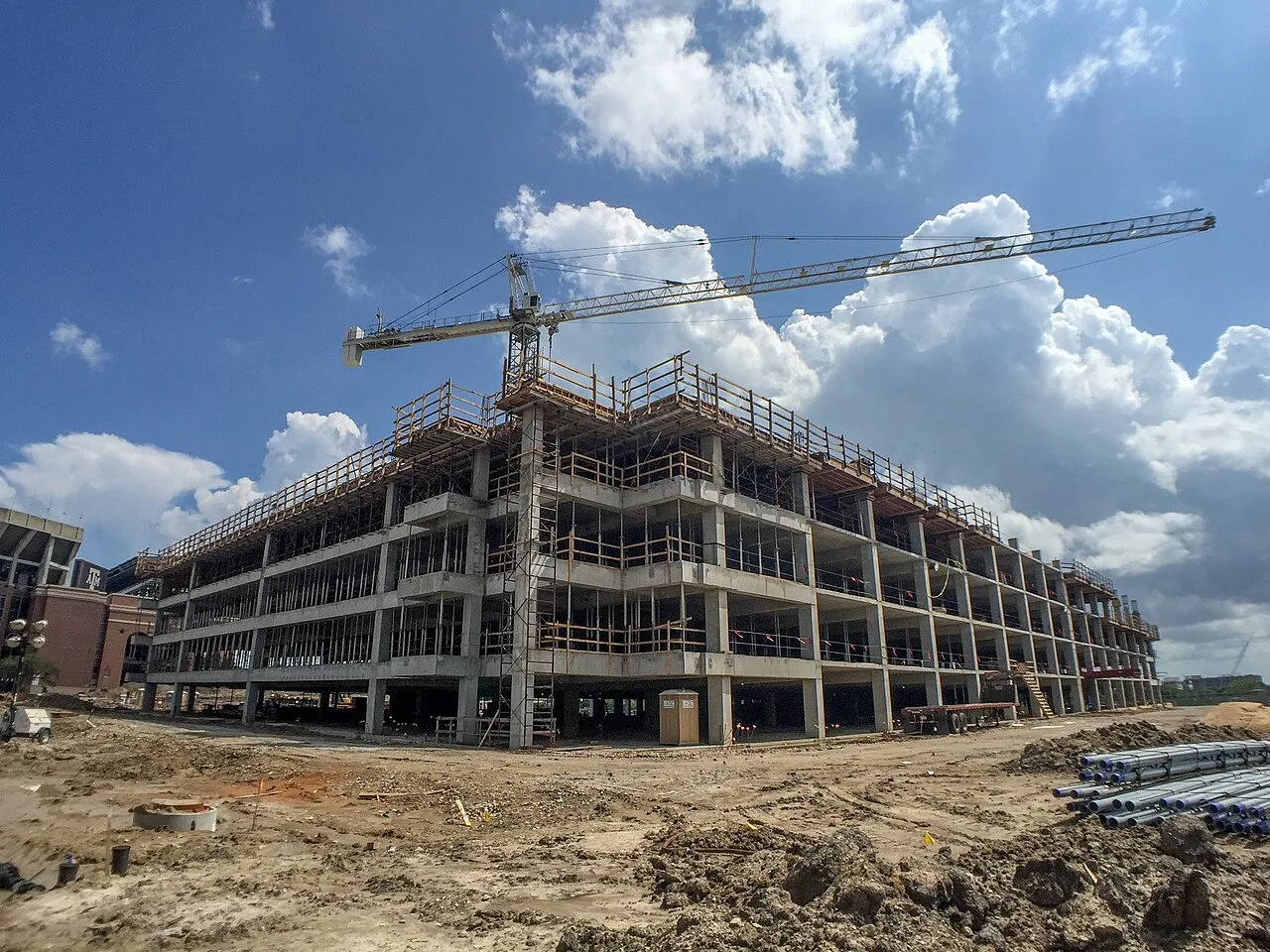 A tower crane over the concrete frame of a building going up on the hotel and conference center site at Texas A&M University in College Station, with pipe stacked on the dirt in front