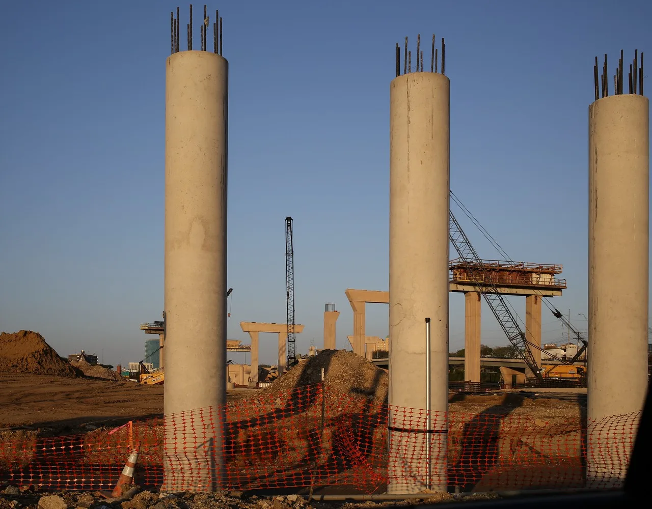 A crawler crane working among new concrete bridge columns on a highway construction site in Fort Worth