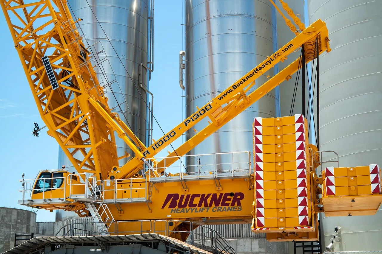 A yellow Liebherr LR 11000 crawler crane with stacked counterweights beside steel tanks at the Starbase launch site at Boca Chica, east of Brownsville