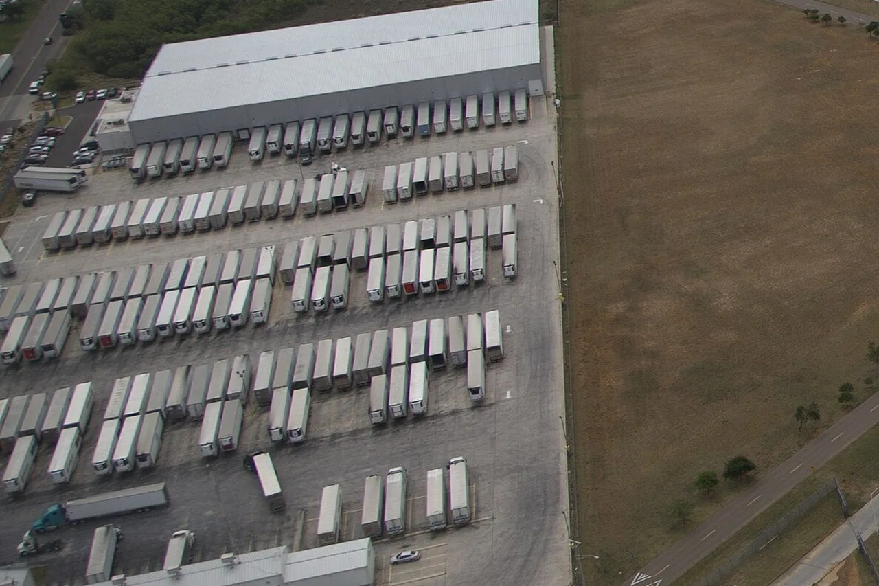 Rows of white semi-trailers backed up to a long warehouse, seen from the air in a set of photos taken at the World Trade Bridge in Laredo