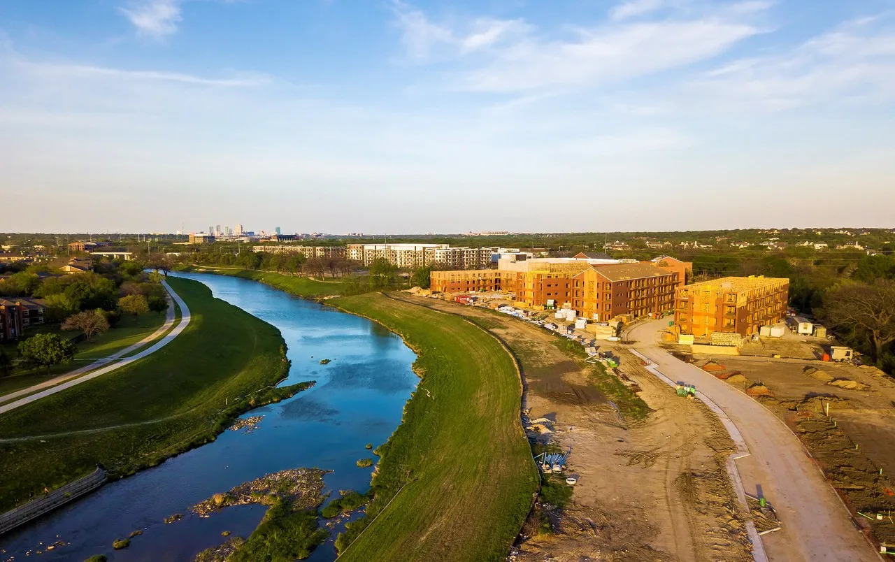 Aerial view of a construction site beside the Clear Fork of the Trinity River, with the downtown Fort Worth skyline on the horizon
