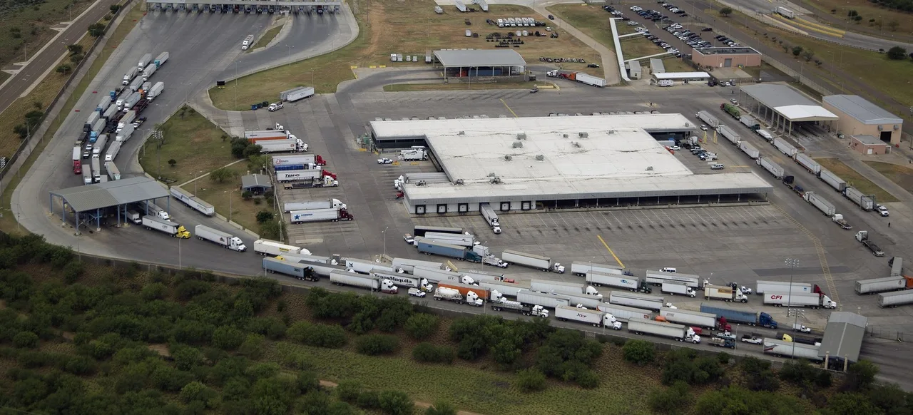 Tractor-trailers in the lanes around a long customs building at the World Trade Bridge in Laredo, seen from the air