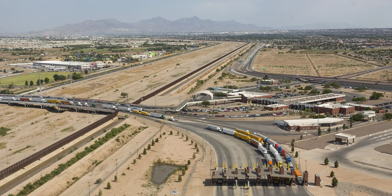 The Ysleta port of entry near El Paso from the air, with a line of tractor-trailers at the booths, the bridge behind and mountains on the horizon