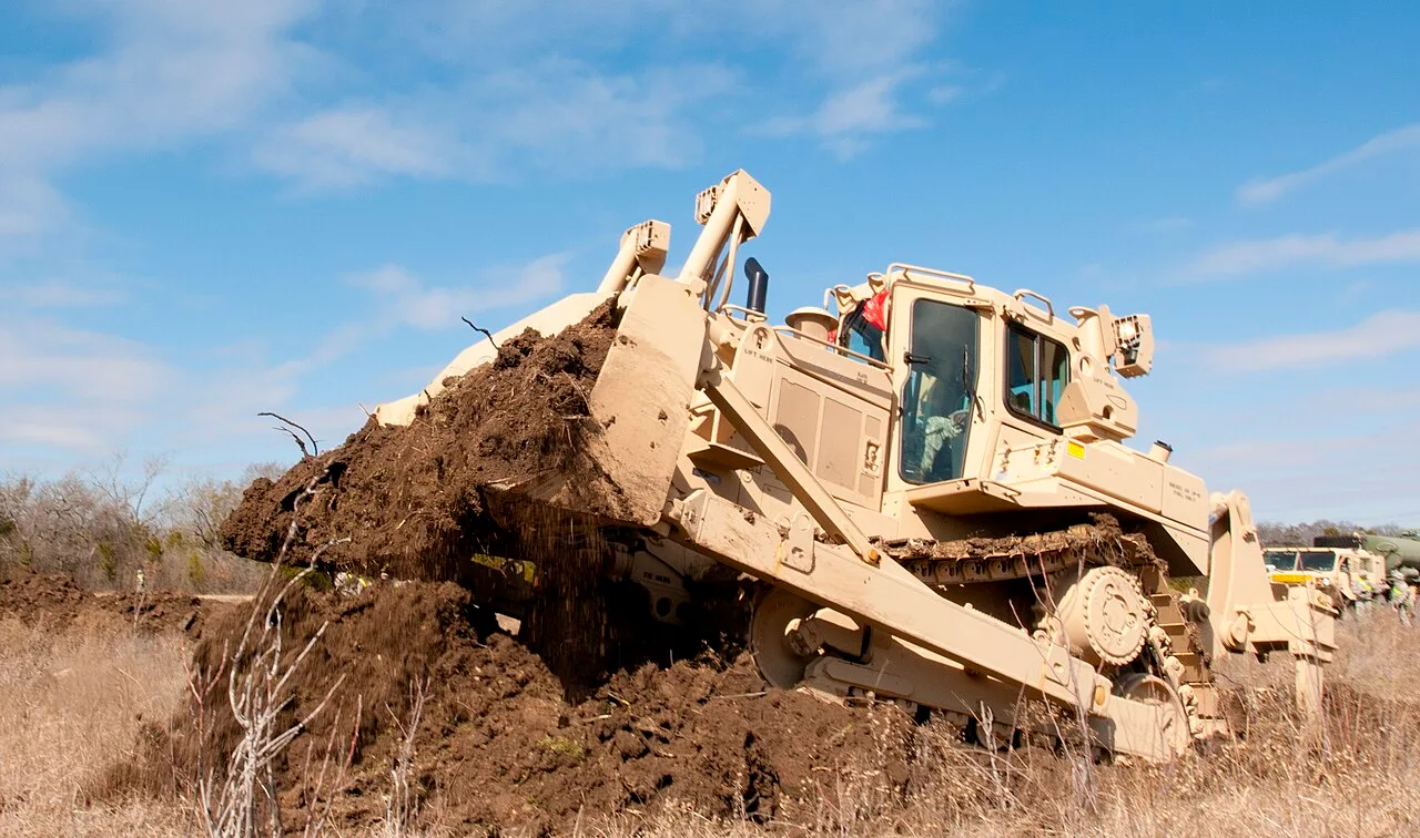 An Army Caterpillar D7 bulldozer pushing a blade full of earth through dry grass at Fort Hood