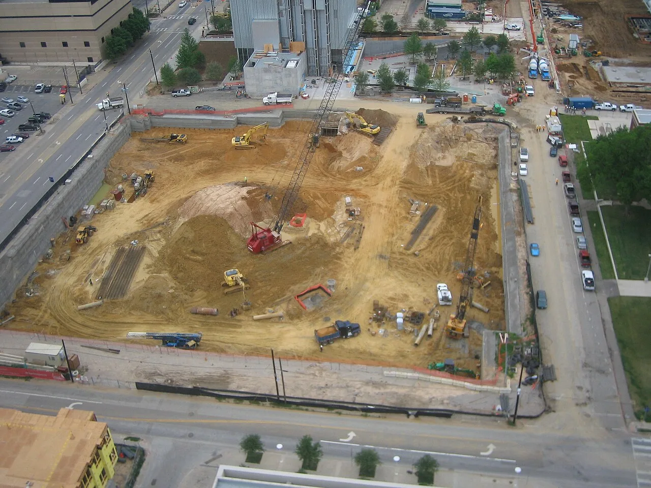 Excavators, a crawler crane and dump trucks working a deep excavation in the Dallas Arts District, seen from above
