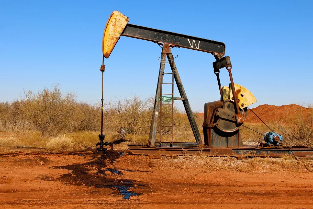 A black and yellow oil well pumping unit on red dirt just east of Electra in Wichita County, with a blue motor on its base and brush behind