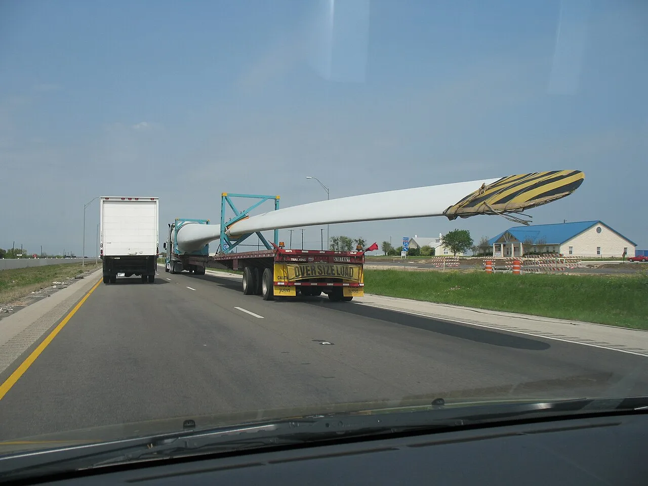 A truck pulling a wind turbine blade on a long trailer marked Oversize Load on Interstate 35 near Elm Mott in McLennan County, seen from the car behind