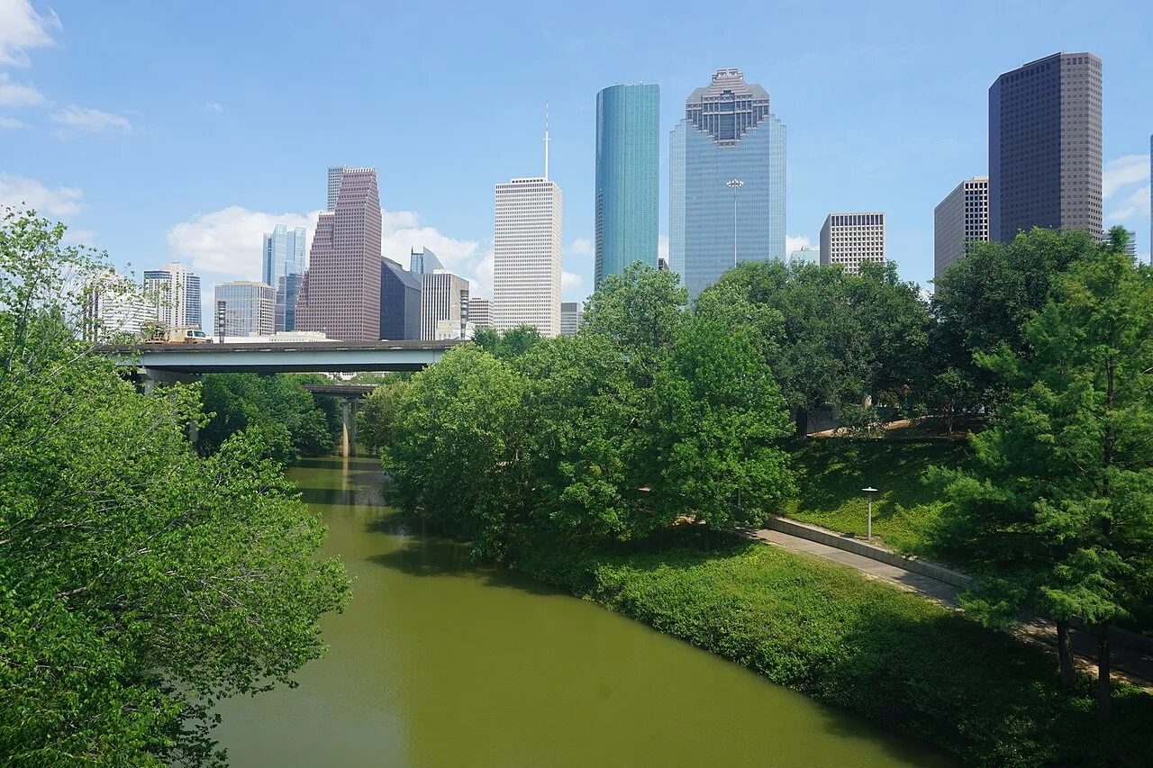 Downtown Houston skyline rising behind Buffalo Bayou and the trees of Buffalo Bayou Park on a clear day